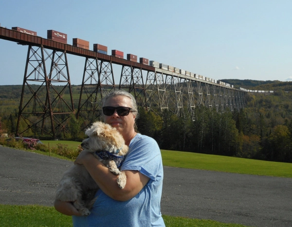 Woman holding dog with train passing overhead